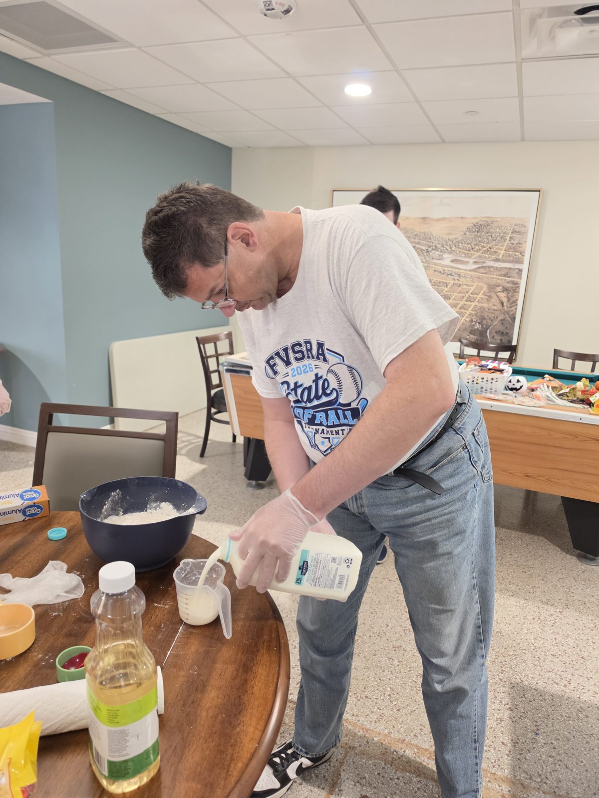 A CAI participant pours milk into a bowl while preparing pancake batter.